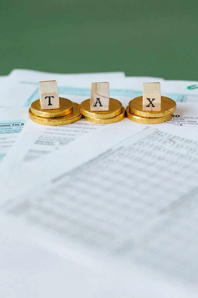 pexels-photo-6863176-6863176 Staged image of gold coins with tax letter tiles on documents.